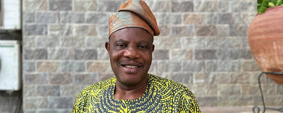 Pa Ayilara lächelt in die Kamera, nachdem er nach Nigeria zurückgekehrt ist, um das Maniok-Anbauunternehmen zu gründen, von dem er schon immer geträumt hatte.